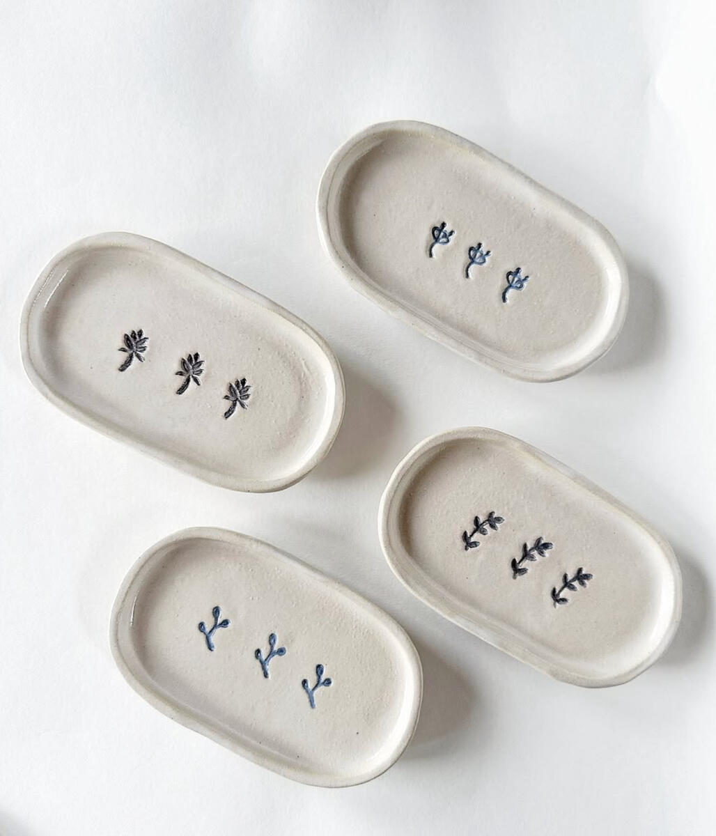 Botanical ceramic soap dishes — handcrafted oval collection from Natty Ceramics atelier in Utrecht Four handcrafted oval ceramic soap dishes with minimalist blue floral stamps on a pale matte surface