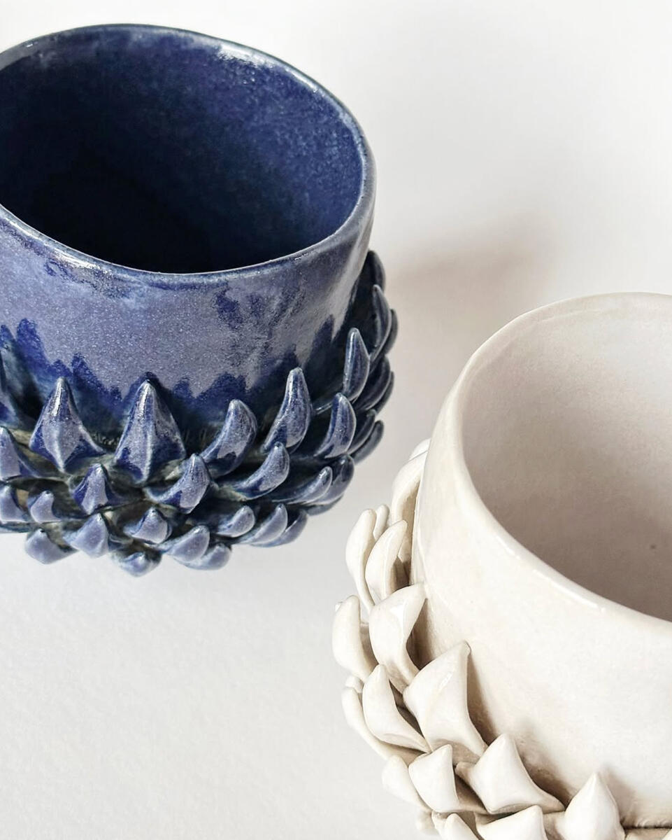 Two handmade ceramic cups with sculpted, artichoke-like texture — one glazed in deep blue, one in soft white Sculpted ceramic cups from Natty Ceramics atelier in Utrecht — handmade elegance in blue and white
