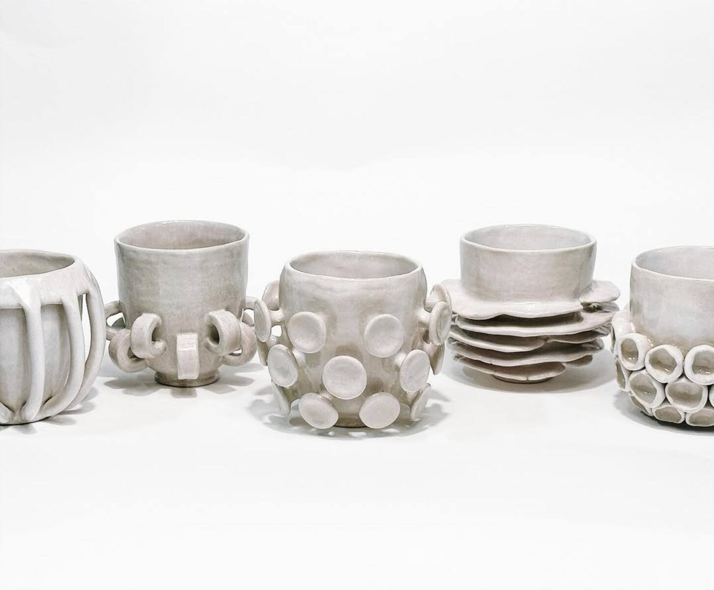 Safe Mugs — sculpted ceramic collection by Natty Ceramics atelier in Utrecht A row of handmade white ceramic mugs and bowls with sculpted, playful textures — part of the “Safe Mugs” series by Natty Ceramics atelier in Utrecht